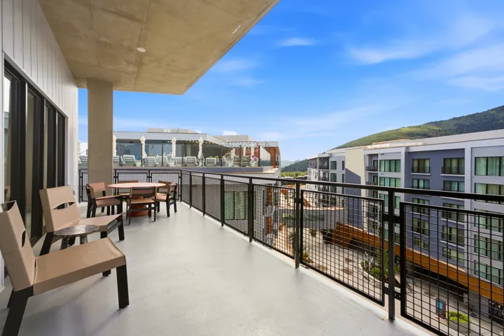 Expansive private balcony with a durable concrete floor, contemporary metal railing, and a clear mountain backdrop
