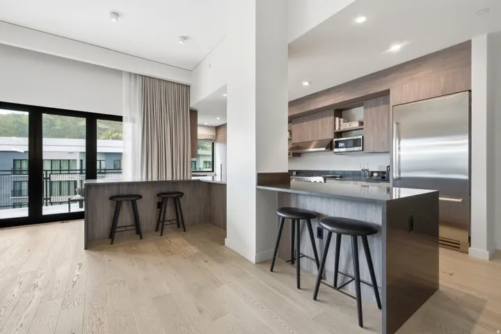 Light wood-finish flooring with a kitchen featuring built-in stainless steel appliances, dark flat-panel cabinetry, and a peninsula with countertop seating