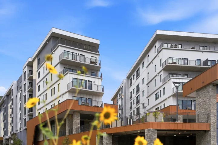 Modern building exterior featuring multiple balconies with glass railings, an integrated parking structure, and stone accents