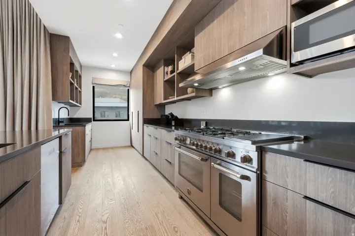 Kitchen featuring wood-finish cabinetry, dark countertops, recessed lighting, and stainless steel appliances including a range with hood, microwave, and dishwasher