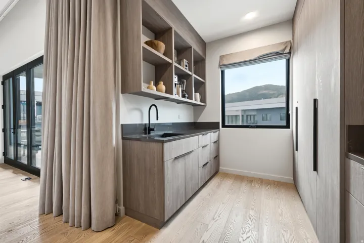 Wood-finish flooring with integrated cabinetry, built-in shelving, and a dark countertop with an undermount sink
