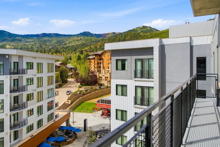 Balcony with metal railing and grating, overlooking multi-story buildings with balconies, and a mountainous landscape