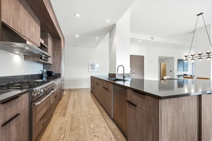 Open-concept kitchen featuring wood-finish cabinetry, stainless steel appliances, a large center island with an integrated sink, and recessed lighting