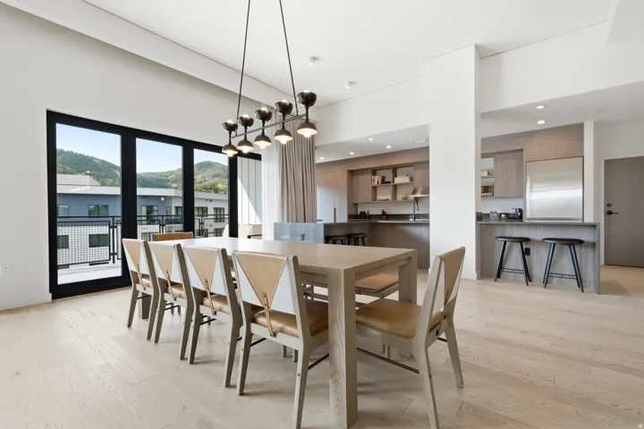 Expansive dining area with light wood-finish flooring, a contemporary linear chandelier, and a black-framed glass door opening to a balcony