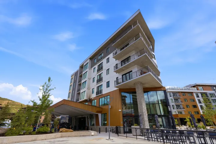 Modern multi-story building featuring expansive glass facades, private balconies with glass railings, and a stone-clad support column