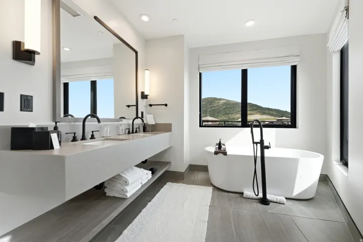 Freestanding soaking tub with a floor-mounted faucet, dual floating vanity with integrated sinks, and black framed windows