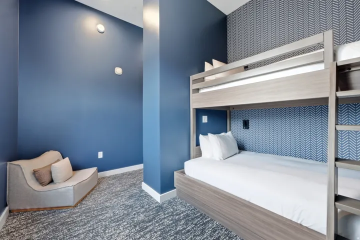 Two-tier bunk bed with a wood-finish frame, accent wallpaper, blue painted walls, and textured carpeting
