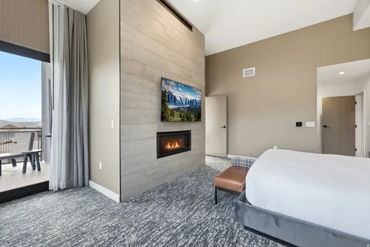 Balcony access with sliding glass door, integrated wall-mounted fireplace, textured accent wall, vaulted ceiling, and patterned carpet flooring
