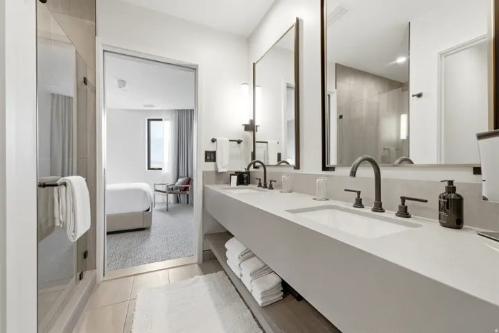 Dual rectangular mirrors with dark frames, a floating dual vanity with integrated sinks, matte black faucets, a glass-enclosed shower, and light-toned tile flooring