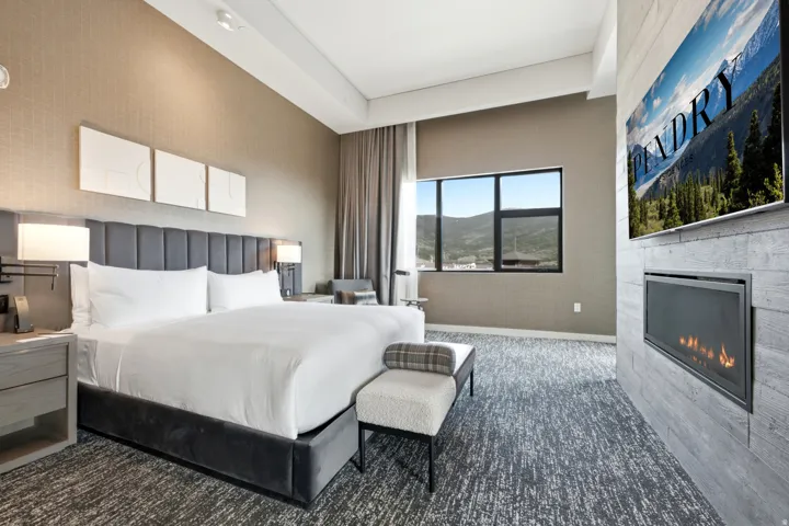 Bedroom with textured accent wall, upholstered headboard, integrated wall sconces, large window, and wall-mounted fireplace