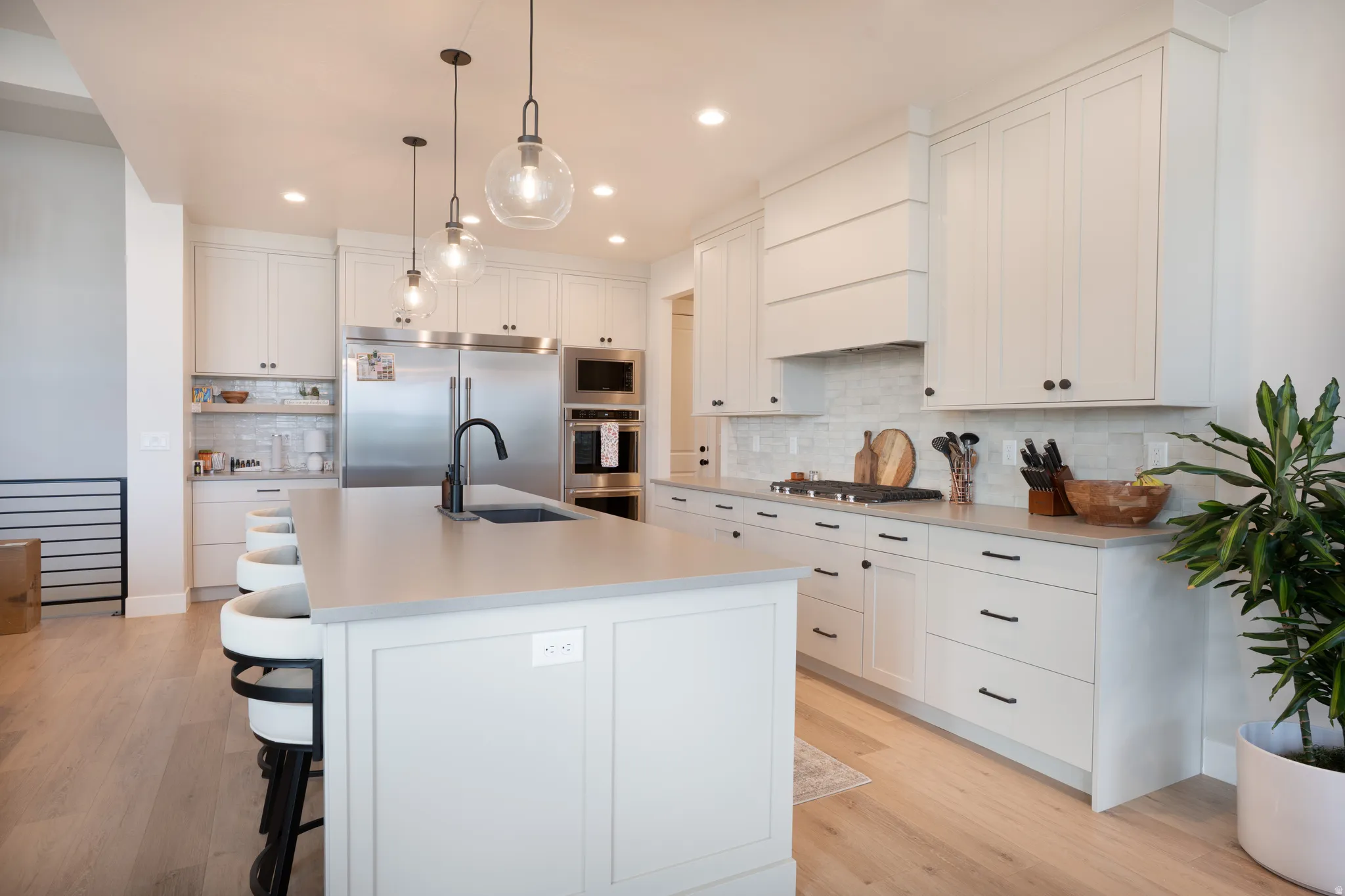 Gourmet kitchen featuring white cabinetry, light countertops, wood-finish flooring, stainless steel appliances, and pendant lighting