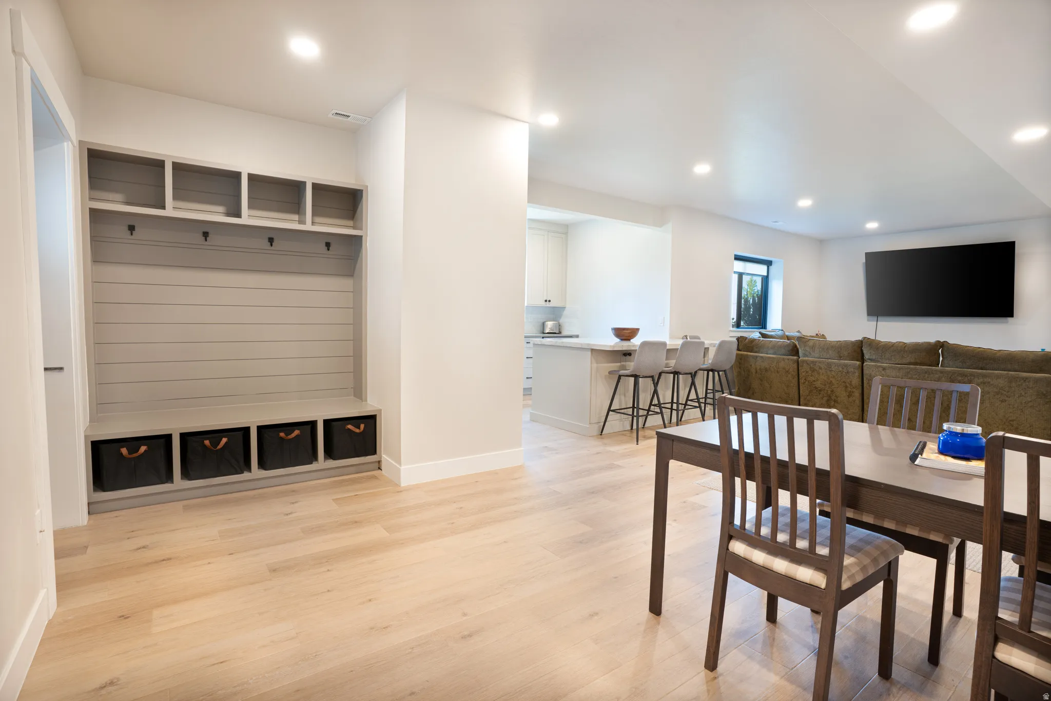 Built-in mudroom storage with bench seating, light wood-finish flooring, recessed lighting, white walls, and a kitchen island with stone countertops