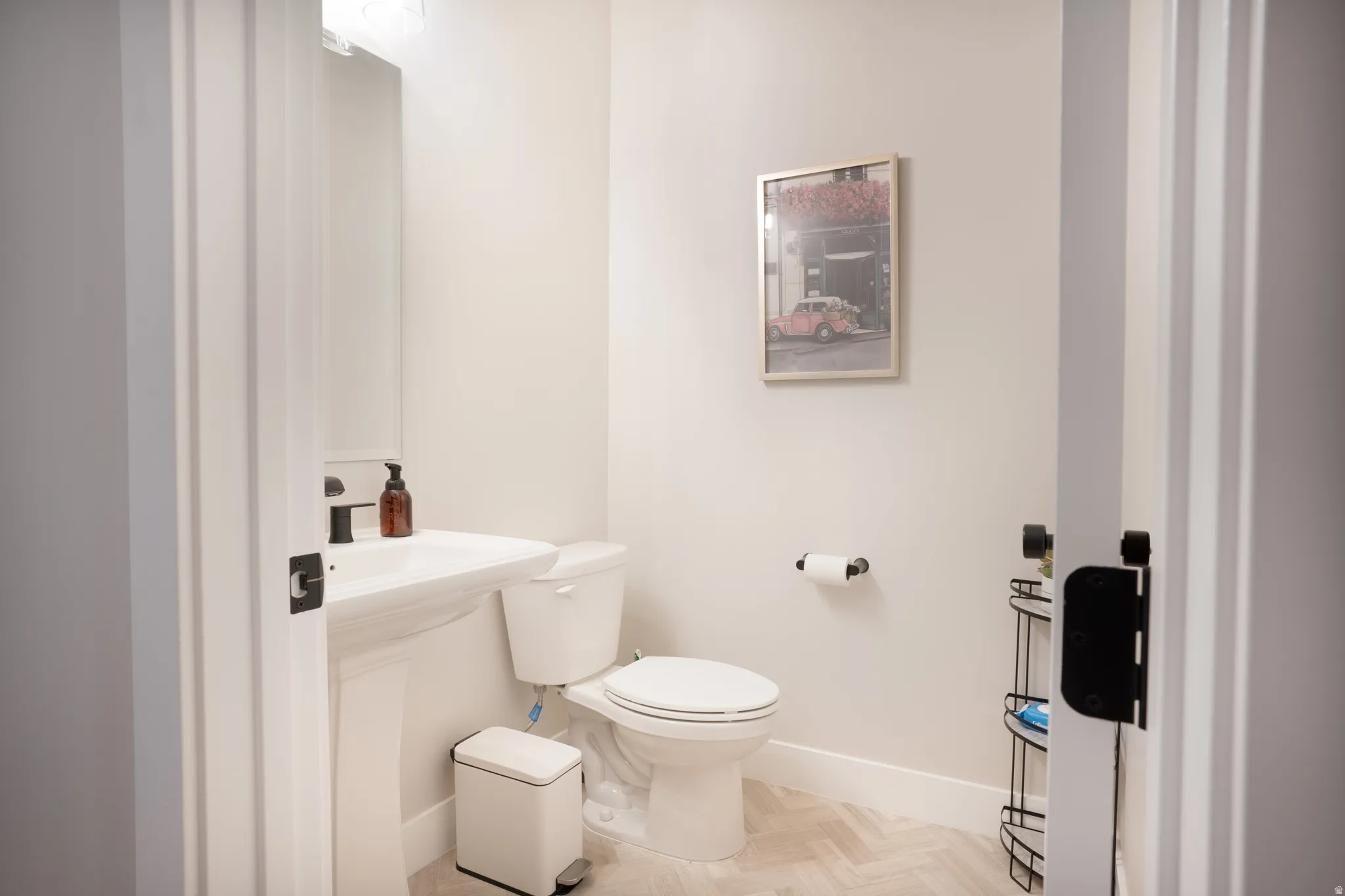 Pedestal sink with a matte black faucet, wall-mounted mirror, and herringbone pattern flooring