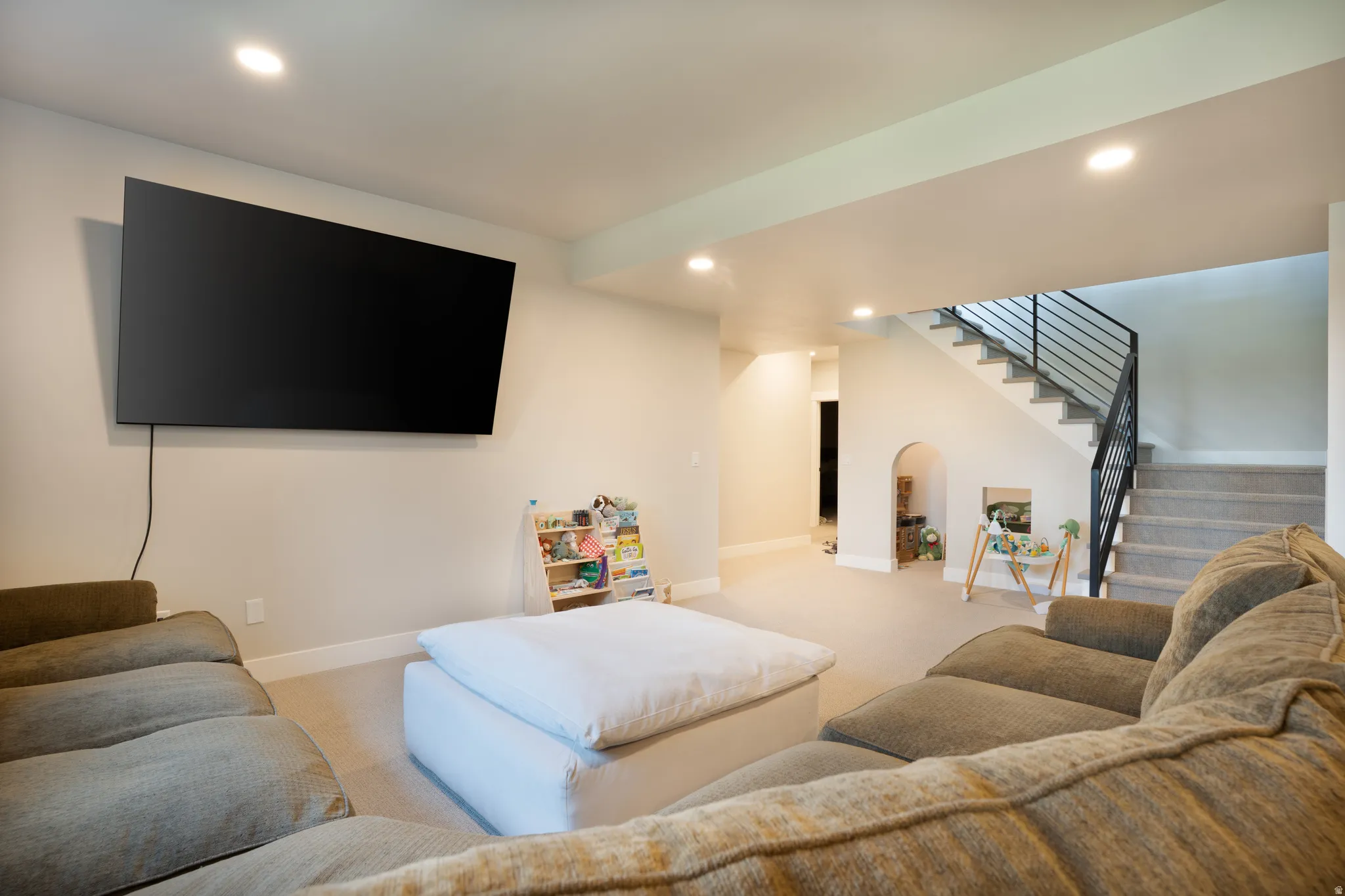 Recessed lighting, wall-mounted television, carpeted flooring, staircase with metal railing, and arched wall niche