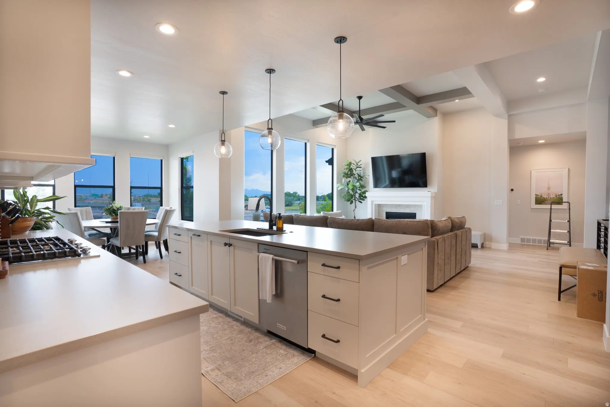 Open-concept living space featuring a kitchen island with pendant lighting, integrated stainless steel appliances, light-toned wood-finish flooring, and a living area with a fireplace