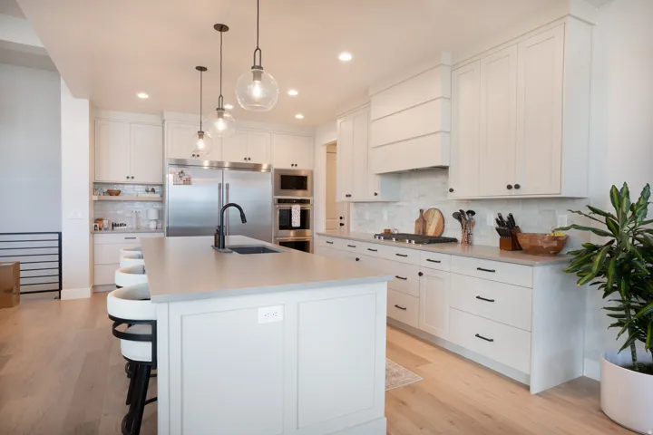 Gourmet kitchen featuring white cabinetry, light countertops, wood-finish flooring, stainless steel appliances, and pendant lighting