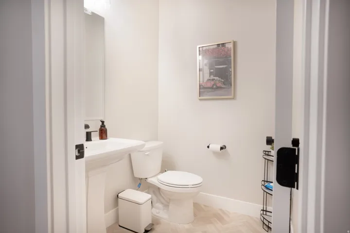 Pedestal sink with a matte black faucet, wall-mounted mirror, and herringbone pattern flooring