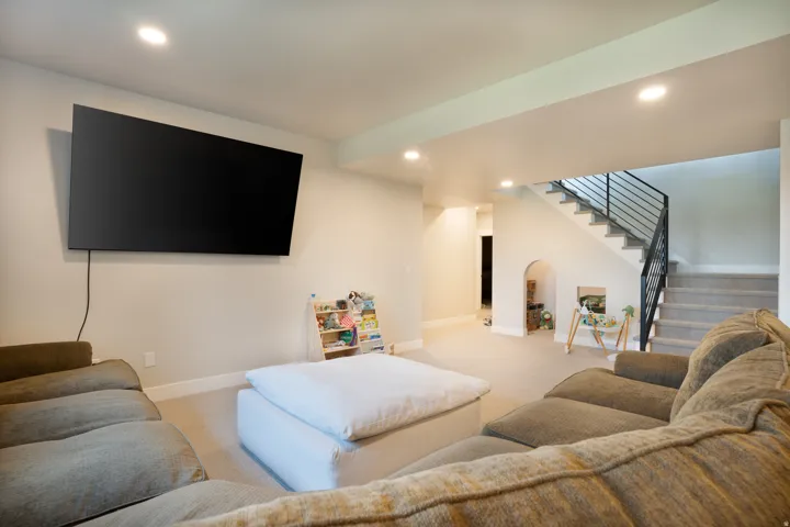 Recessed lighting, wall-mounted television, carpeted flooring, staircase with metal railing, and arched wall niche