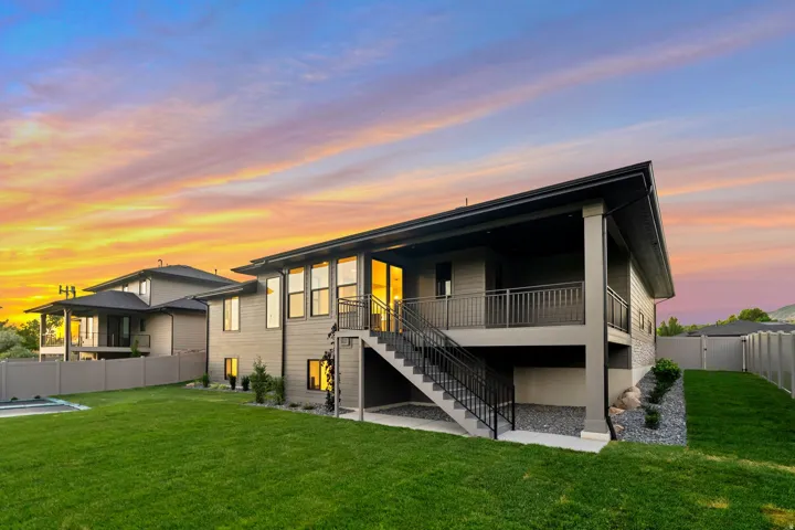 Expansive backyard featuring a manicured lawn, covered patio, exterior stairs with metal railings, and a fenced perimeter