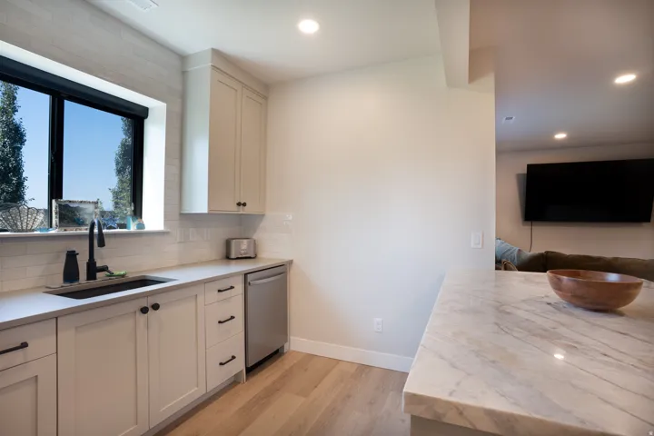 Kitchenette featuring a stainless steel dishwasher, undermount sink with a matte black faucet, light wood-finish flooring, and light-toned cabinetry