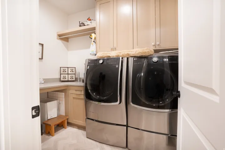 Laundry area featuring wood-finish cabinetry, light-toned countertops, and light-toned flooring in a herringbone pattern