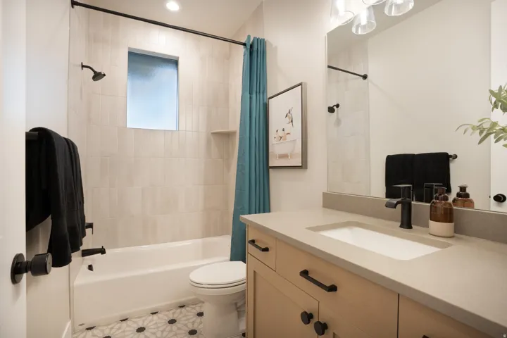 Bathroom featuring a shower/tub combination with tiled surround, a built-in shower niche, a wood-finish vanity with a single sink, and patterned floor tiling