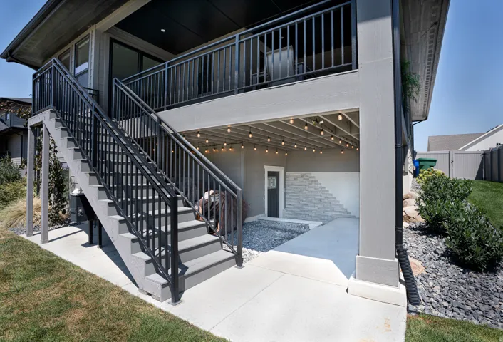 Two-story exterior with a ground-level patio featuring decorative string lights, an upper-level balcony, and a dedicated staircase with black metal railings
