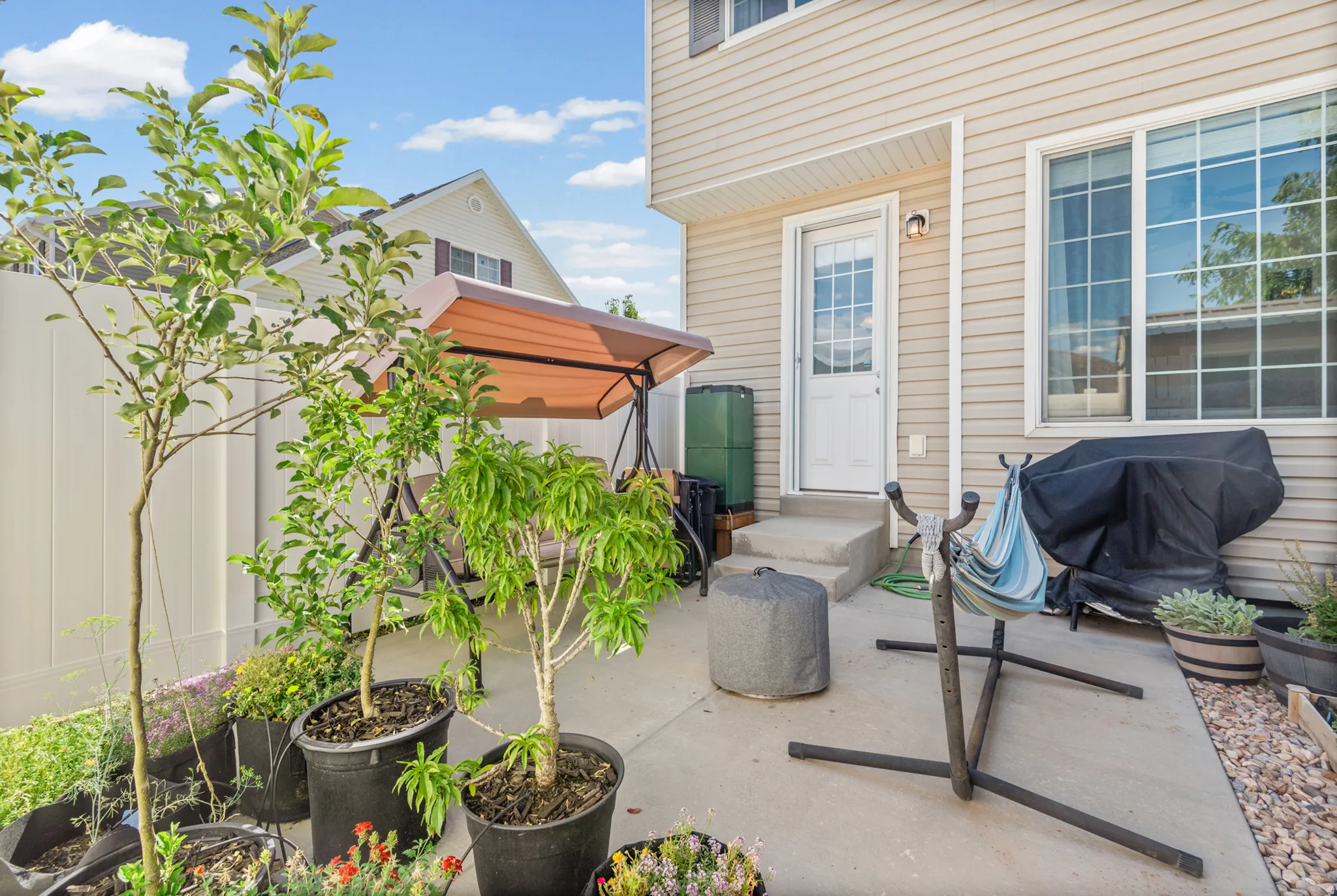Concrete patio area with a white privacy fence, light-colored siding, and a glass-paneled exterior door