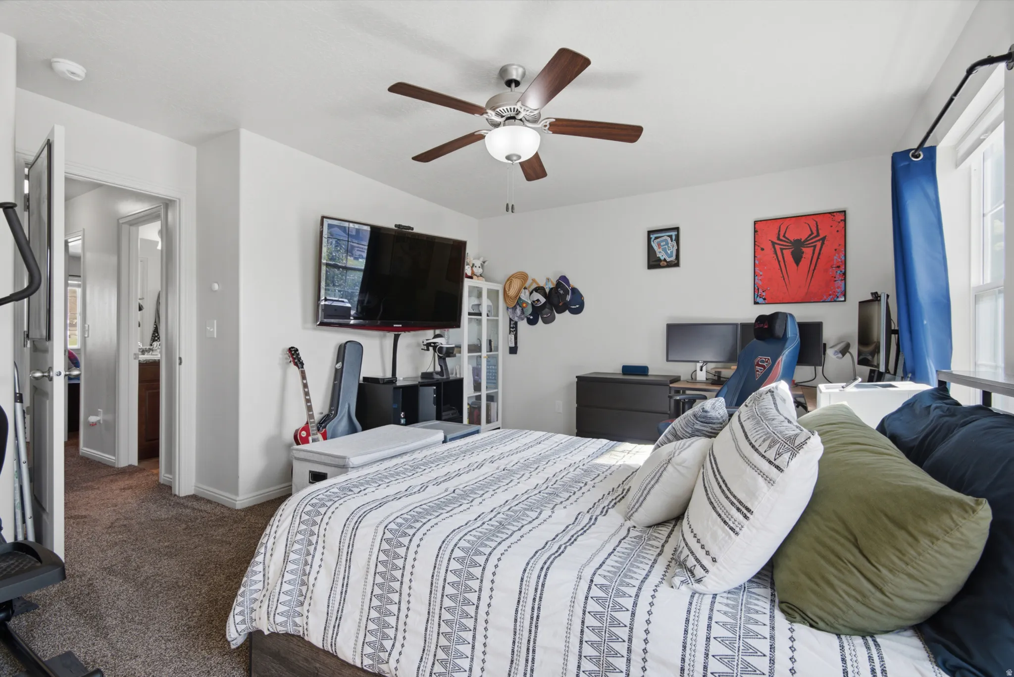 Carpeted room with a ceiling fan, wall-mounted television, and a window