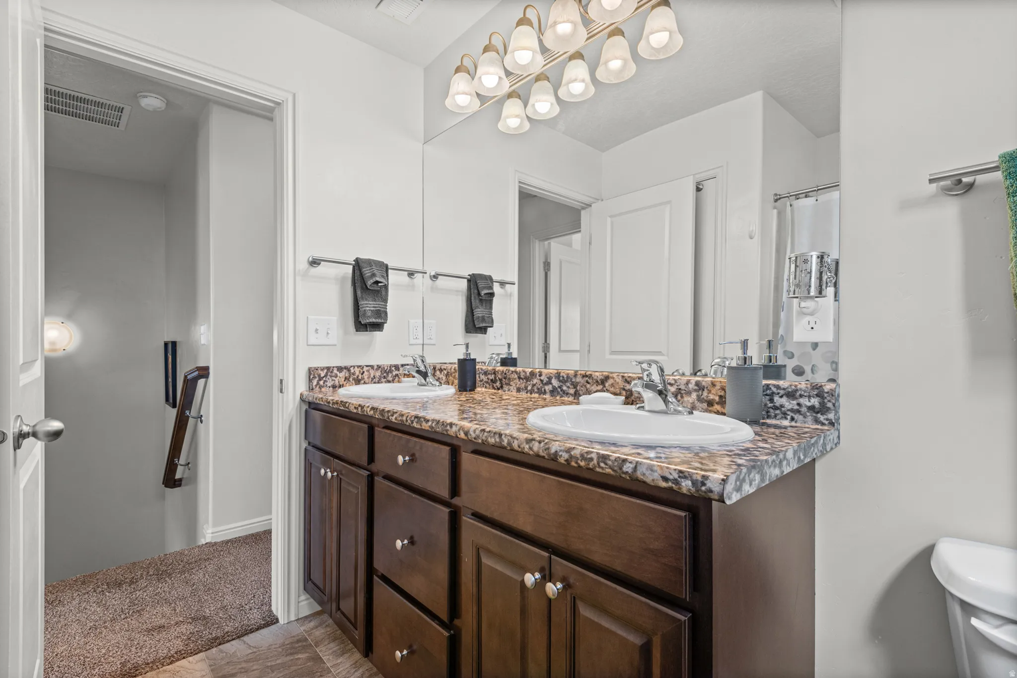 Dual undermount sinks with chrome fixtures, a spacious vanity featuring dark wood-finish cabinetry, and a large wall-mounted mirror with overhead lighting