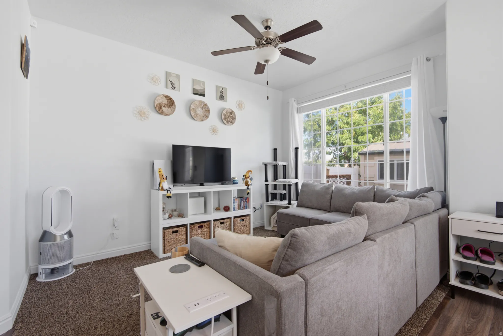 Light-filled living area featuring a large multi-pane window, ceiling fan with integrated lighting, and carpeted flooring