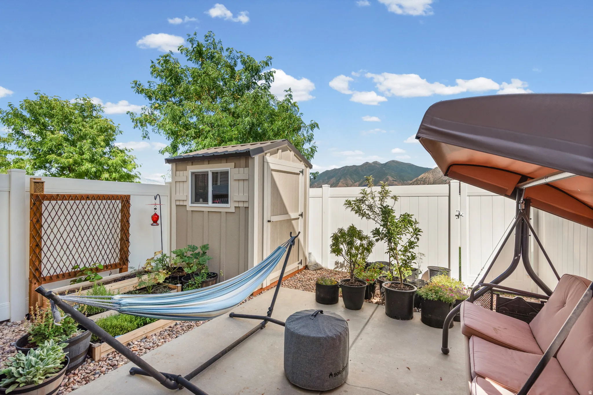 Paved patio area featuring a storage shed, white privacy fencing, and a built-in planter box