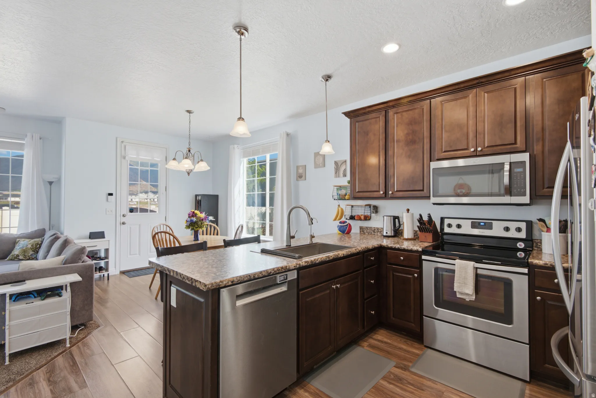 Kitchen featuring wood-finish flooring, dark wood cabinetry, stainless steel appliances, and a kitchen island with stone-finish countertops