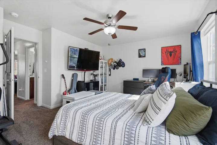 Carpeted room with a ceiling fan, wall-mounted television, and a window