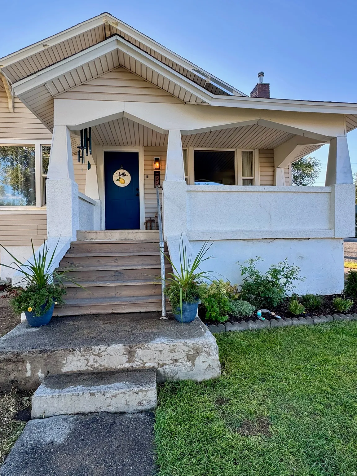 Covered front porch with wood stairs, a deep blue entry door, and a landscaped planting bed