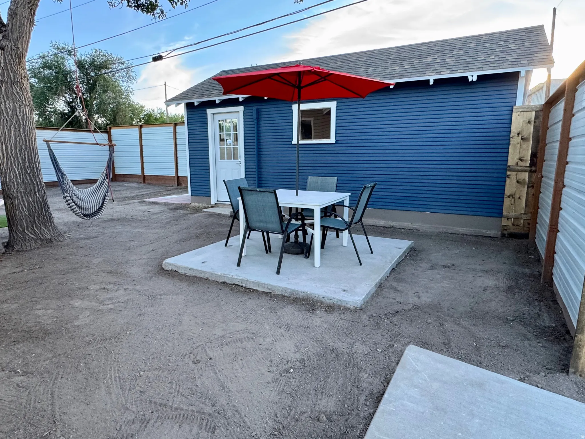 Outdoor entertaining space featuring a concrete patio with dining table and chairs, red cantilever umbrella for shade, huge mature tree and swing ,