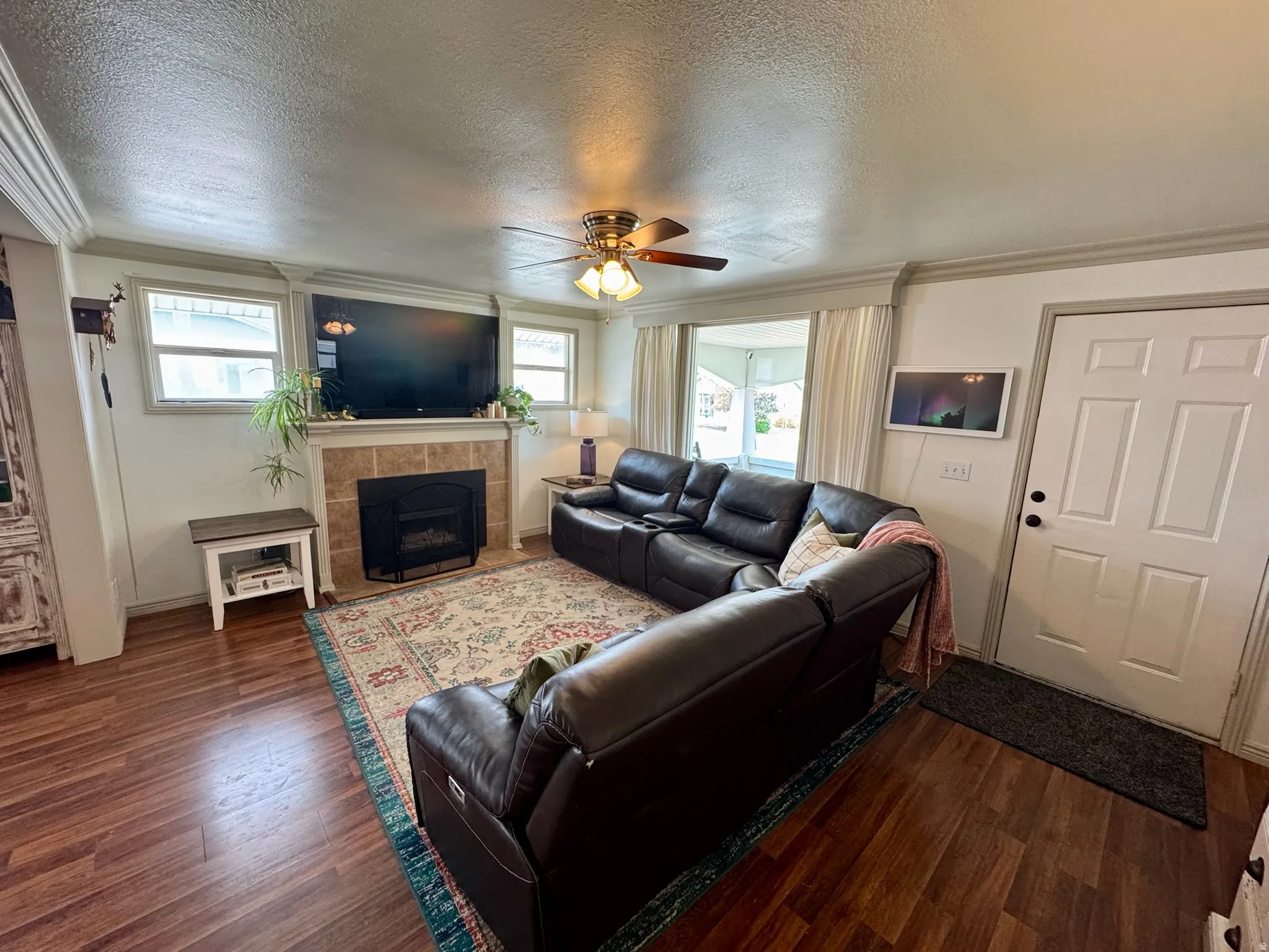 Living area with wood-finish flooring, a ceiling fan with integrated lighting, and a tiled fireplace
