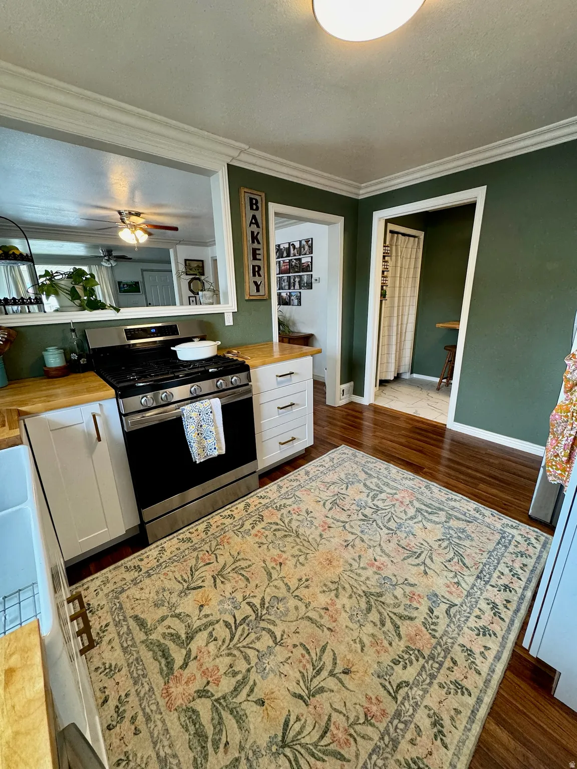 Hardwood flooring, stainless steel range, white shaker-style cabinetry, wood-finish countertops, crown molding