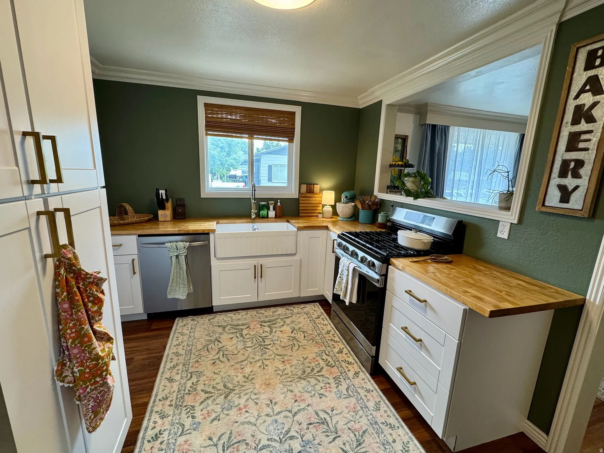 Kitchen featuring wood-finish custom countertops, white cabinetry with gold-tone hardware, a white farmhouse sink, and stainless steel appliances