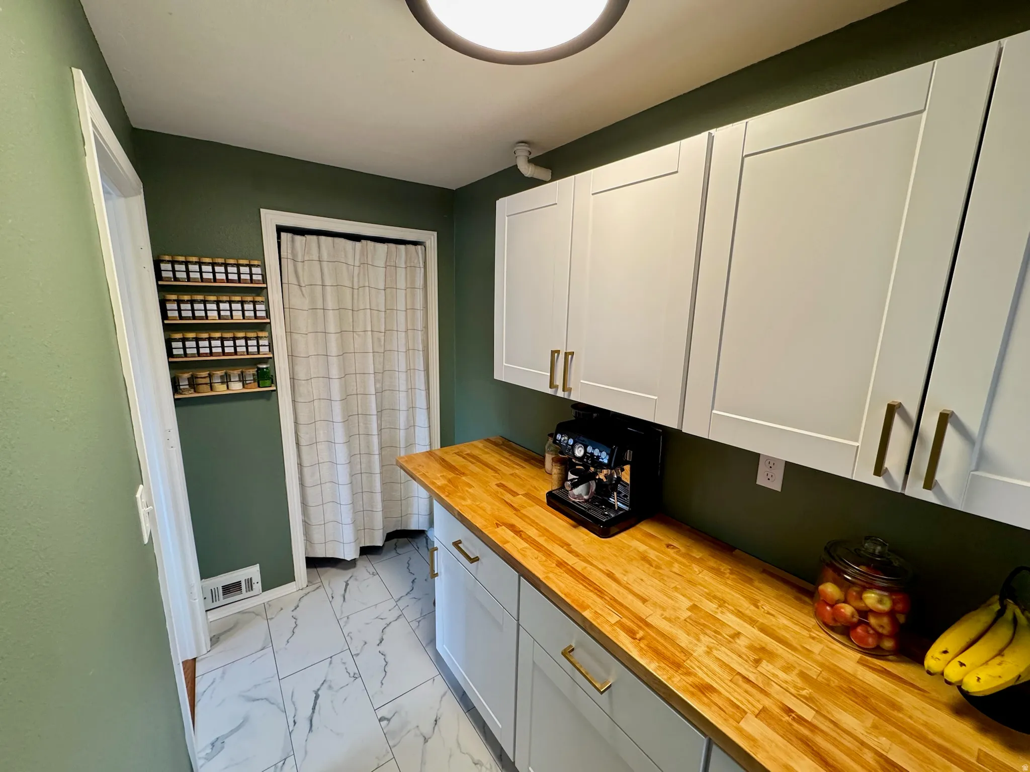 Butlers Pantry. White shaker-style cabinetry with gold-tone hardware, wood-finish countertops, and white rectangular tile flooring