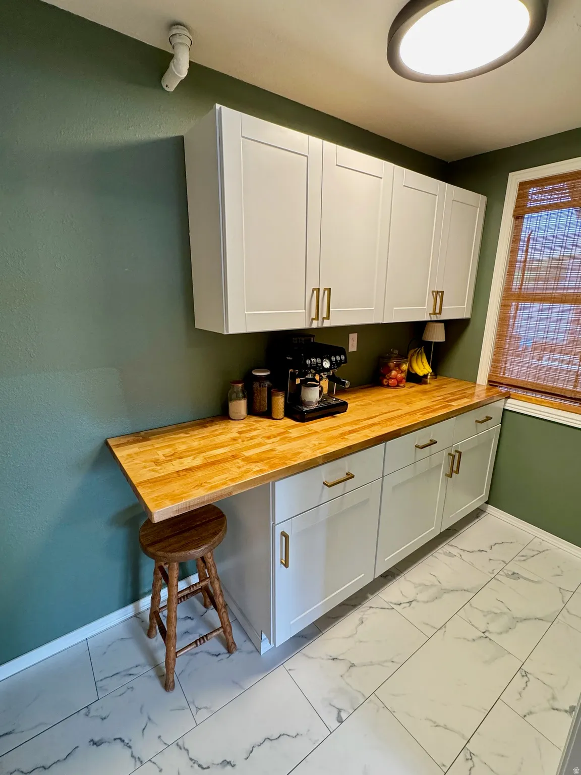 White shaker-style cabinetry with gold-tone hardware, wood-finish countertops, and large format tile flooring