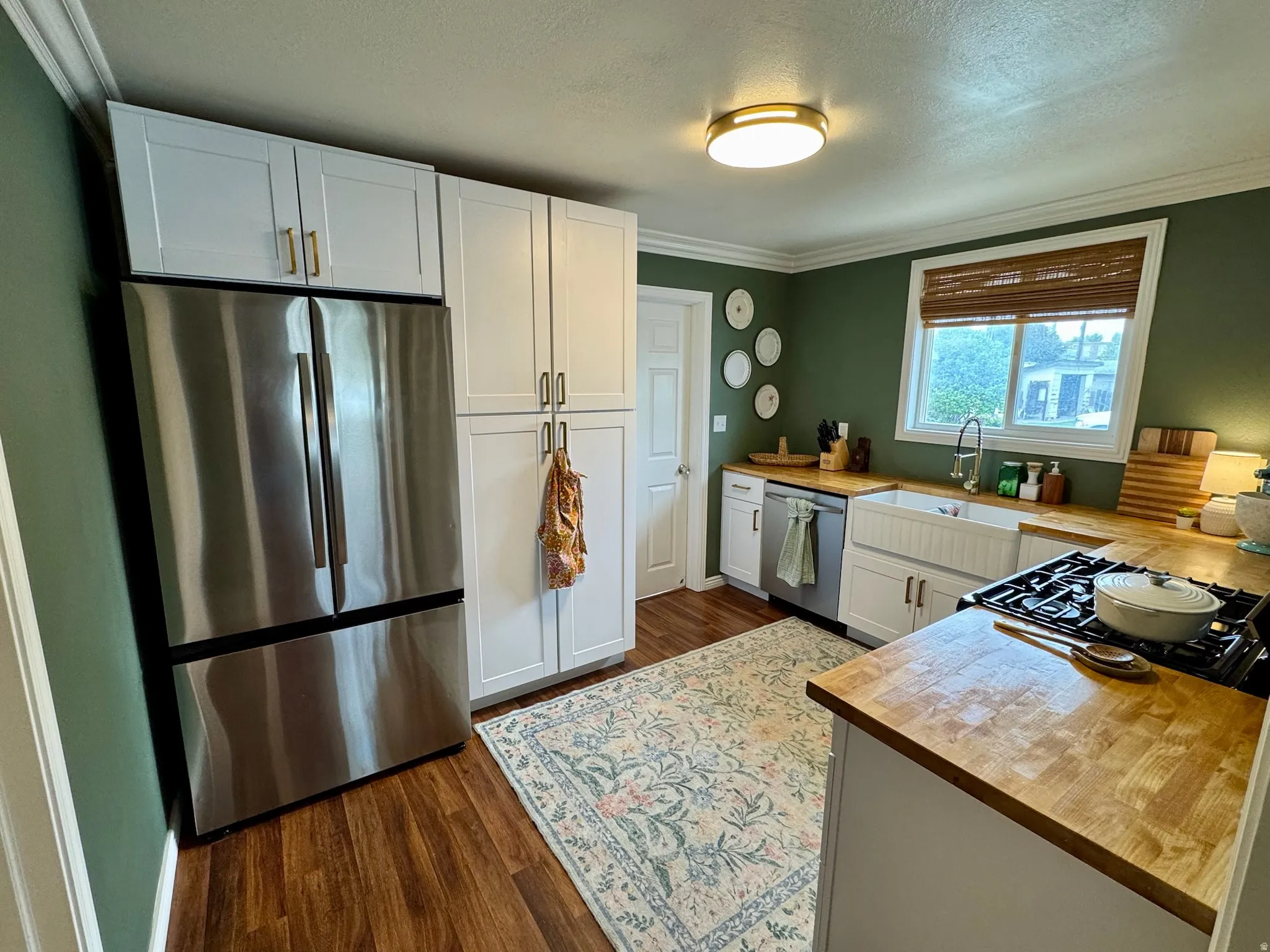 Stainless steel refrigerator, white shaker-style cabinetry, custom wood-finish countertops, apron-front sink, and wood-finish flooring
