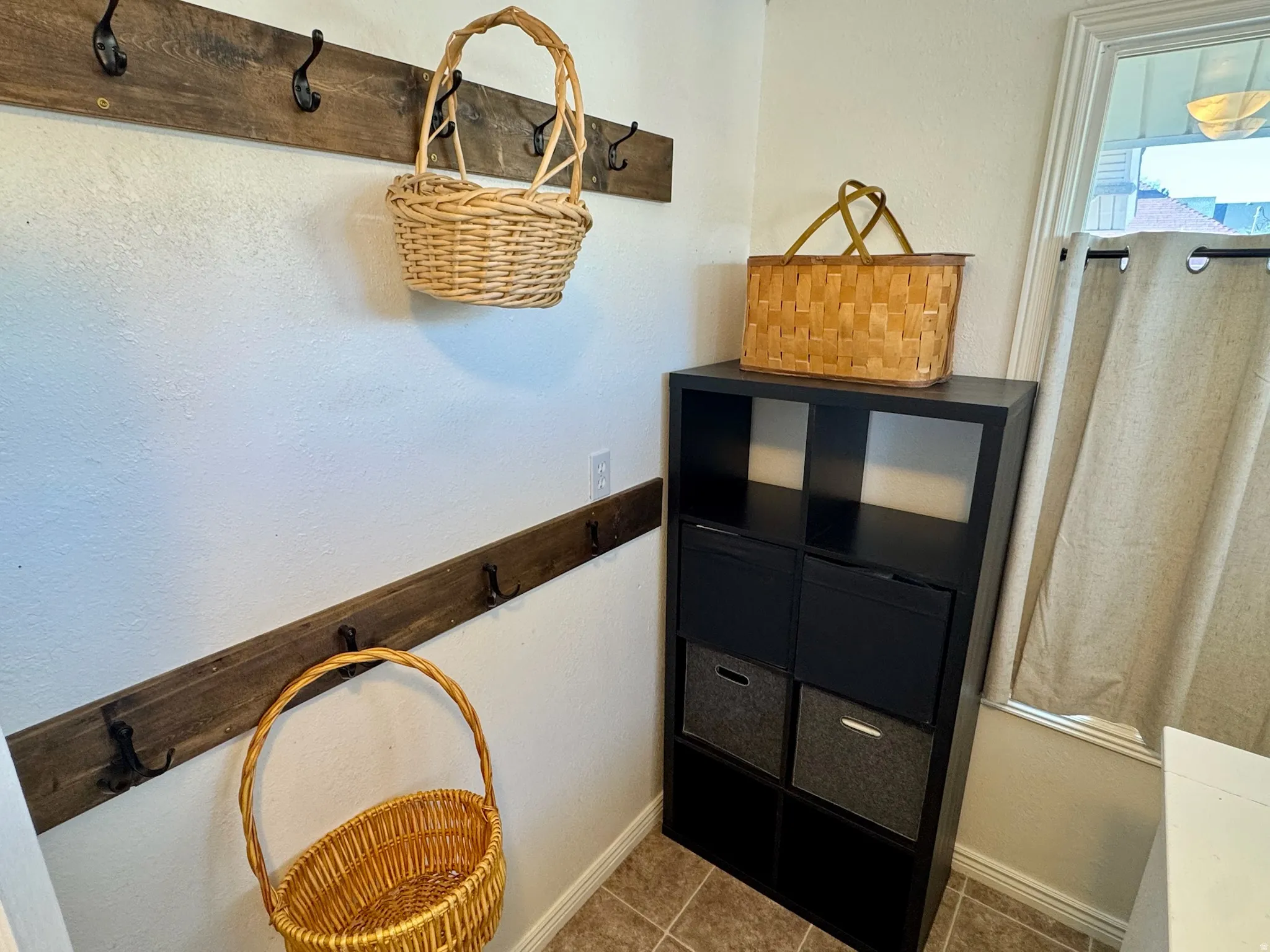 Wall-mounted wood-finish coat racks with black hooks and a multi-pane window