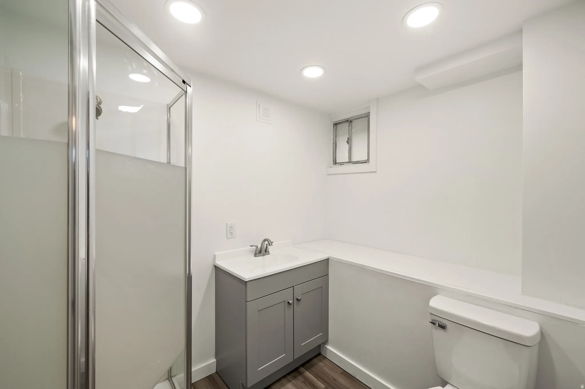 Shower with framed frosted glass enclosure, gray vanity with integrated sink, wood-finish flooring, and recessed lighting