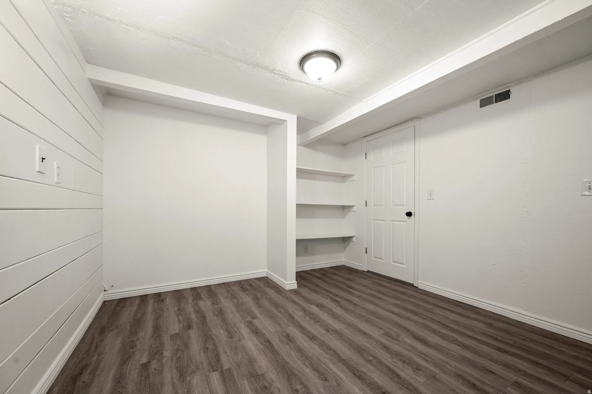 Wood-finish flooring, built-in shelving, white paneled walls, and a ceiling-mounted light fixture