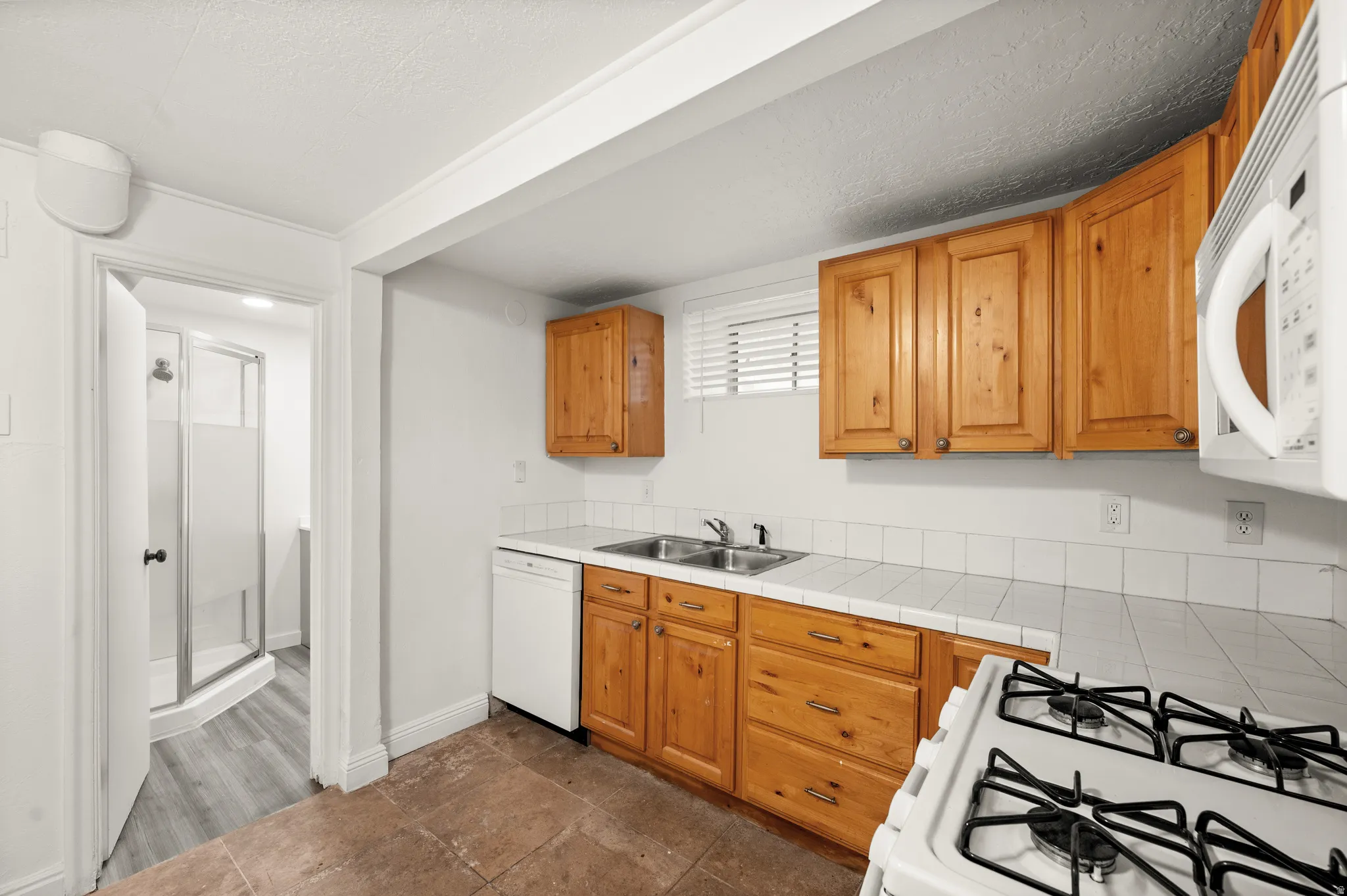 Kitchenette with wood-finish cabinetry, tile countertops, and a white tile backsplash