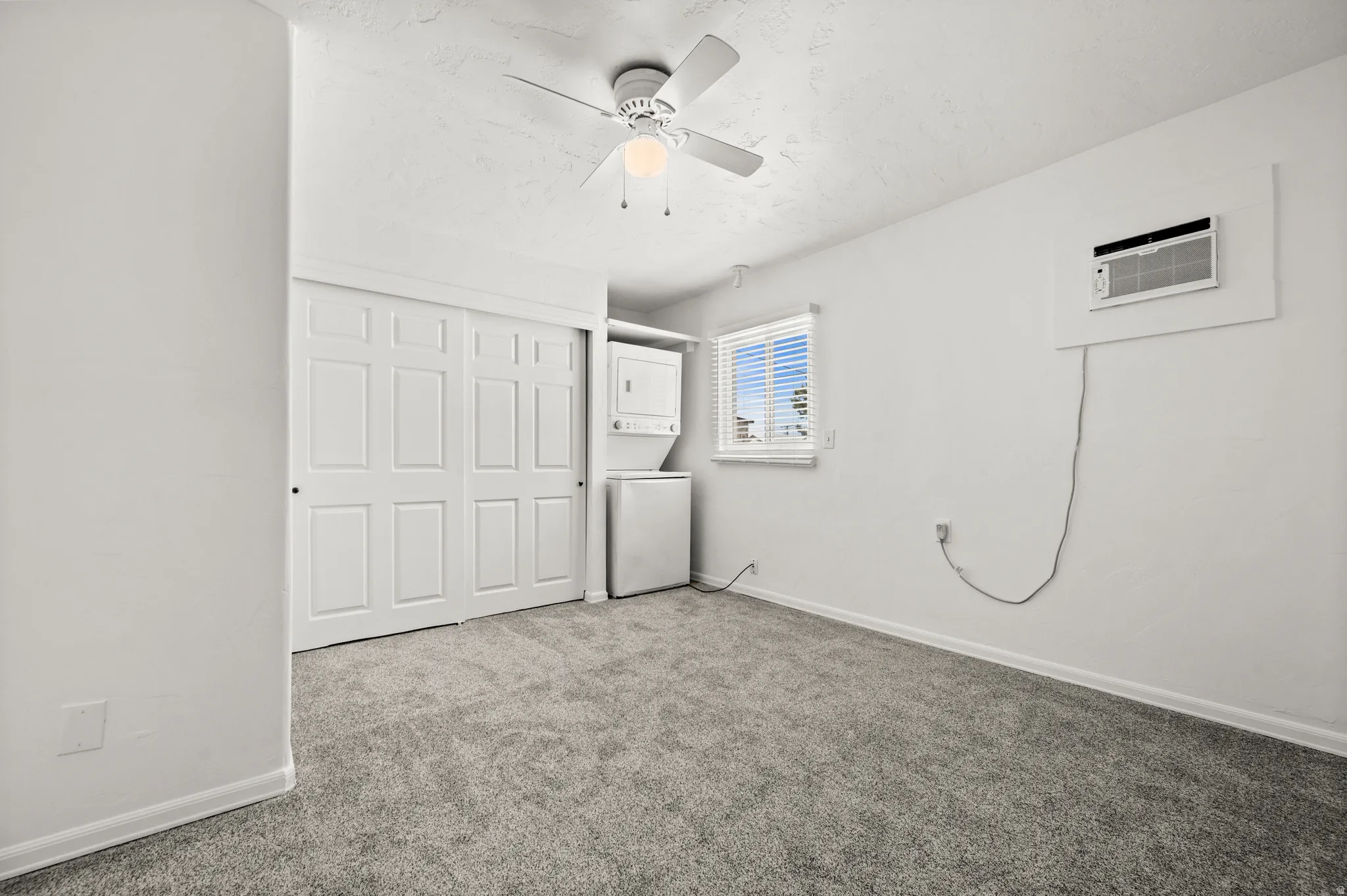 Wall-mounted air conditioning unit, ceiling fan with integrated lighting, built-in window with blinds, and white sliding closet doors