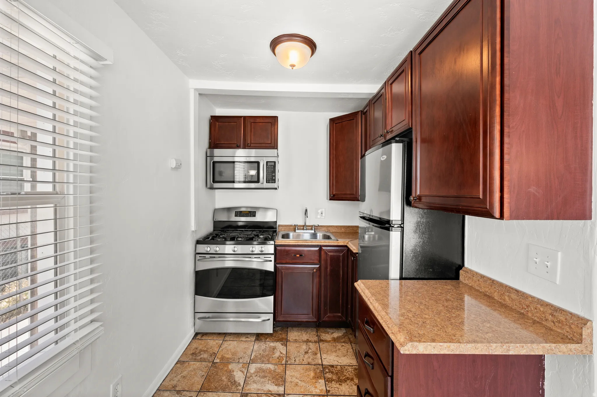 Kitchen featuring wood-finish cabinetry, stainless steel appliances, speckled countertops, and tiled flooring