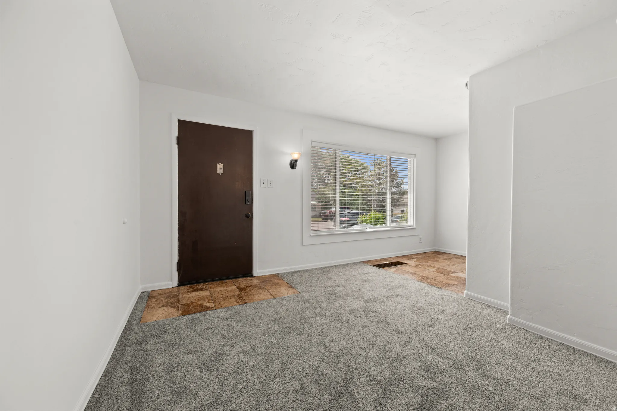 Entryway featuring a dark wood-finish door, sconce lighting, and a window with blinds