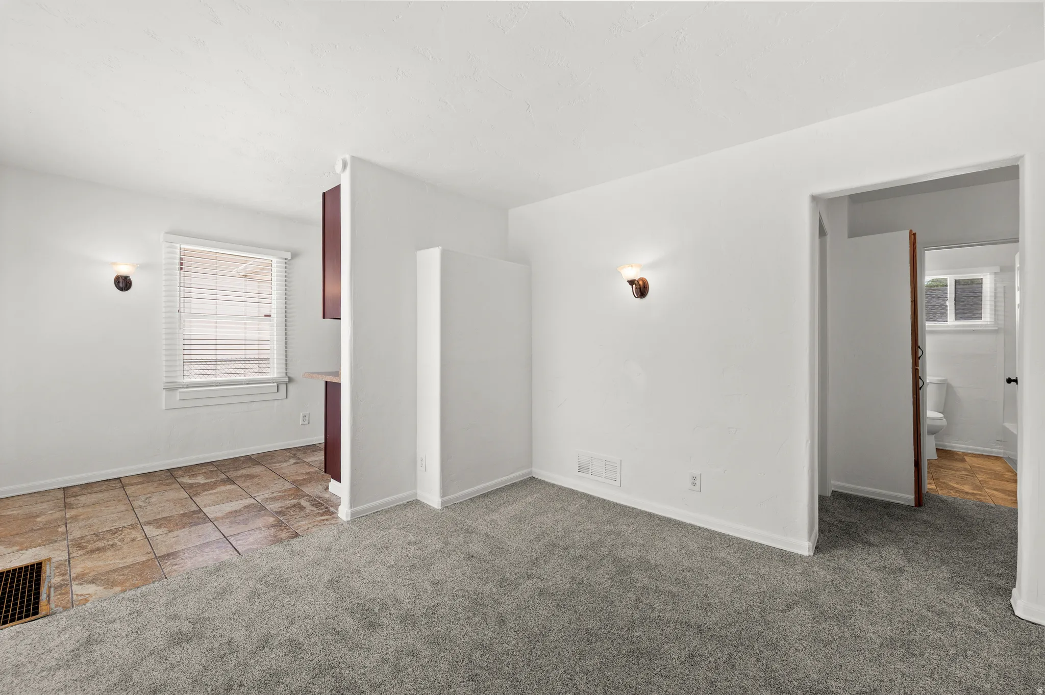 Neutral wall color with wall-mounted sconces, plush grey carpeting, and a tiled floor area